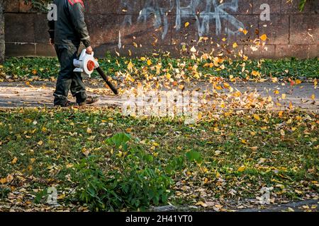 Trockene Blätter mit einer Windmühle reinigen. Ein kommunaler Arbeiter säubert den Stadtpark. Stadtparks für den Winter vorbereiten. Stockfoto