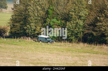 Der Land Rover Defender 110 parkte auf einem Rasenplatz mit angrenzendem Copse und nahm Hunde für ihren täglichen Übungsweg mit, Wiltshire UK Stockfoto