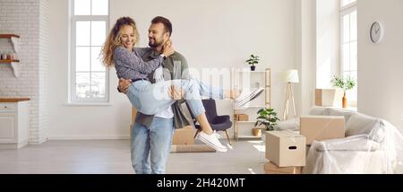 Glücklicher, liebevoller Ehemann, der seine geliebte Frau während des Umzugsvorgangs in seinem neuen Haus in den Armen hält. Stockfoto