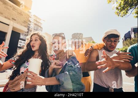 Tanzen in der Stadt. Eine Gruppe von Freunden der Generation z singt und tanzt, während sie in der Sommersonne gemeinsam spazieren gehen. Glückliche junge Freunde, die Spaß haben, während Stockfoto