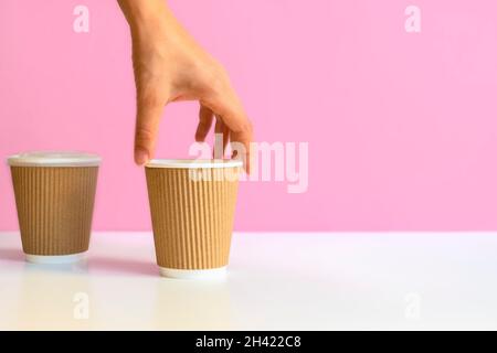 Die Hand der Frau nimmt eine Papierkaffeetasse vom weißen Tisch. Bild mit Kopierplatz, Zero Waste Konzept Stockfoto