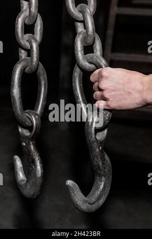 Die Hand eines Arbeiters hält in einer Industrieanlage eine eiserne Kette mit einem Hakenhebemechanismus eines Krans. Stockfoto