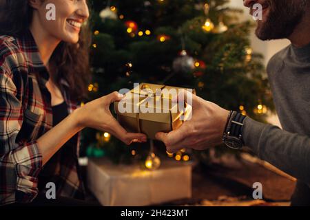 Nahaufnahme eines Paares, das eine Geschenkbox in der Hand hält und einen Weihnachtsbaum im Hintergrund. Glückliches Paar feiert Weihnachten zusammen mit Geschenken. Stockfoto