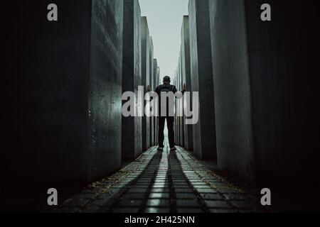 Oktober 2021 - Berlin, Deutschland. Der Mensch steht in einem dunklen Labyrinth zwischen hohen Blöcken im Holocaust-Jüdischen Mahnmal für ermordete Juden. Licht am Ende des Tunnels. Stockfoto