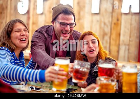 Eine Gruppe von glücklichen Freunden, die im Pub Bierkrüge vom Fass klirren - lächelnde Jungen und Mädchen mit Bier in den Händen beim Toasten im Restaurant in der Happy Hour Stockfoto