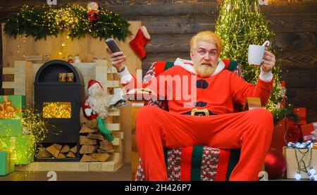 Der weihnachtsmann sitzt im Sessel und trinkt Kaffee. Frohe Weihnachten. Werbung für das neue Jahr. Stockfoto