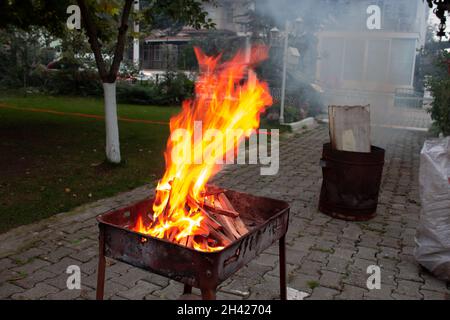 Gestapelte Holzstücke in einem Grill, der in einem orangefarbenen Feuer brennt. Vorbereitung auf den Grill in der Nacht. Abendessen. Stockfoto