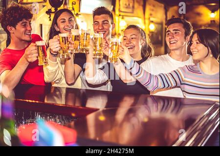 Eine Gruppe von glücklichen Leuten, die an der Theke Bier trinken und toasten - hübsche Teenager-Freunde lächeln, während sie Becher mit Bier vom Fass anklirren - Freundschaft Stockfoto