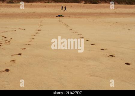 Ein tiefer Blick über den Sand in Polin Bay, Sutherland, Schottland, zeigt zwei Personen, die gehen, tiefe Fußabdrücke im Sand und einen Haufen Kleidung Stockfoto