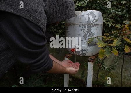Mann dreht den Wasserhahn auf einem weißen Plastikwassersammelfass im grünen Garten an. Stockfoto