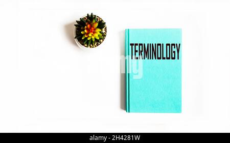 Das Wort Terminologie, geschrieben auf einem grünen Notizbuch und isoliertem weißem Hintergrund, in der Nähe ist eine Kaktusblume Stockfoto