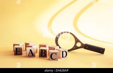 Buchstaben Hintergrund. Holzwürfel mit Buchstaben auf gelbem Hintergrund und mit einer Lupe im Hintergrund Stockfoto