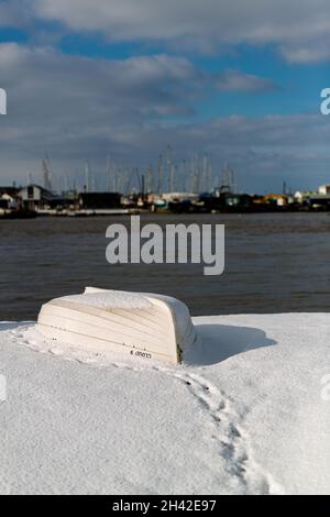 Umgedrehte Ruderboote wurden am Strand an der Küste von Suffolk vertäut. Sie wurden mit Schnee bedeckt, nachdem ein seltener Schneesturm das Gebiet bedeckt hatte Stockfoto