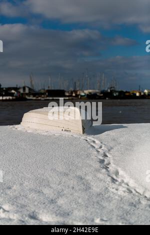 Umgedrehte Ruderboote wurden am Strand an der Küste von Suffolk vertäut. Sie wurden mit Schnee bedeckt, nachdem ein seltener Schneesturm das Gebiet bedeckt hatte Stockfoto