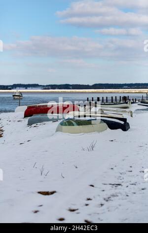Umgedrehte Ruderboote wurden am Strand an der Küste von Suffolk vertäut. Sie wurden mit Schnee bedeckt, nachdem ein seltener Schneesturm das Gebiet bedeckt hatte Stockfoto