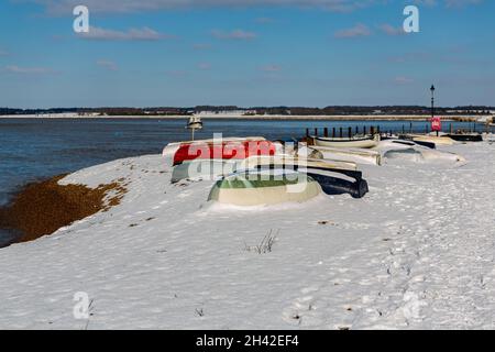 Umgedrehte Ruderboote wurden am Strand an der Küste von Suffolk vertäut. Sie wurden mit Schnee bedeckt, nachdem ein seltener Schneesturm das Gebiet bedeckt hatte Stockfoto