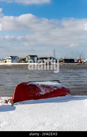 Umgedrehte Ruderboote wurden am Strand an der Küste von Suffolk vertäut. Sie wurden mit Schnee bedeckt, nachdem ein seltener Schneesturm das Gebiet bedeckt hatte Stockfoto