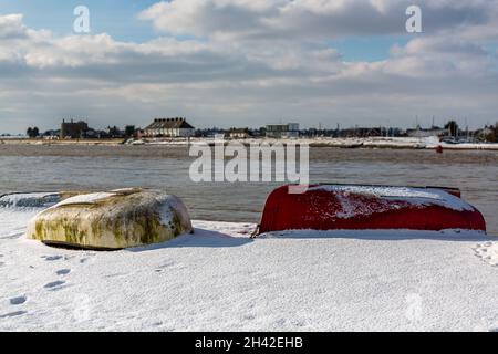 Umgedrehte Ruderboote wurden am Strand an der Küste von Suffolk vertäut. Sie wurden mit Schnee bedeckt, nachdem ein seltener Schneesturm das Gebiet bedeckt hatte Stockfoto