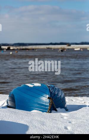 Umgedrehte Ruderboote wurden am Strand an der Küste von Suffolk vertäut. Sie wurden mit Schnee bedeckt, nachdem ein seltener Schneesturm das Gebiet bedeckt hatte Stockfoto