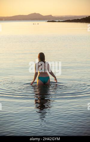 Eine Frau, die bei Aberdour bei einem kalten, aber immer noch aufgehenden Sonnenaufgang im Oktober ins Meer eintrat Stockfoto