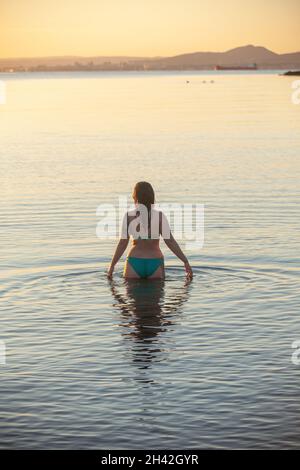 Eine Frau, die bei Aberdour bei einem kalten, aber immer noch aufgehenden Sonnenaufgang im Oktober ins Meer eintrat Stockfoto