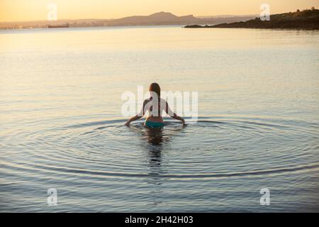 Eine Frau, die bei Aberdour bei einem kalten, aber immer noch aufgehenden Sonnenaufgang im Oktober ins Meer eintrat Stockfoto