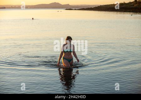 Eine Frau, die einen Bikini trägt und nach einem kalten Wasserschwimmen im Firth of Forth aus dem Meer läuft. Stockfoto