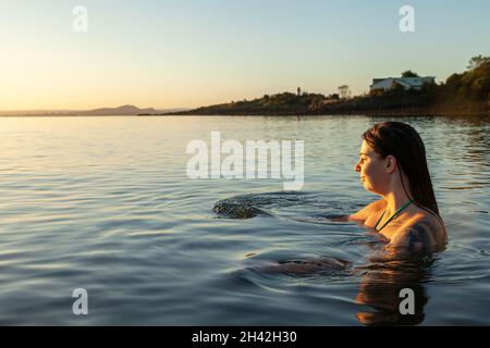 Eine junge schottische Frau, die im Oktober bei Sonnenaufgang im Meer bei Aberdour in Fife, Schottland, schwimmt Stockfoto