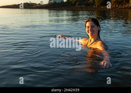 Eine junge schottische Frau, die im Oktober bei Sonnenaufgang im Meer bei Aberdour in Fife, Schottland, schwimmt Stockfoto