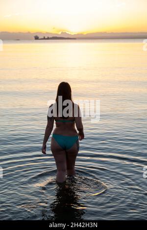 Eine Frau, die bei Aberdour bei einem kalten, aber immer noch aufgehenden Sonnenaufgang im Oktober ins Meer eintrat Stockfoto