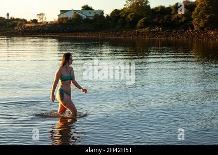 Eine Frau, die einen Bikini trägt und nach einem kalten Wasserschwimmen im Firth of Forth aus dem Meer läuft. Stockfoto