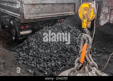 Der LKW-Industrietransport entlädt neben dem Hebemechanismus des Krans einen Stapel Kokskohle. Stockfoto