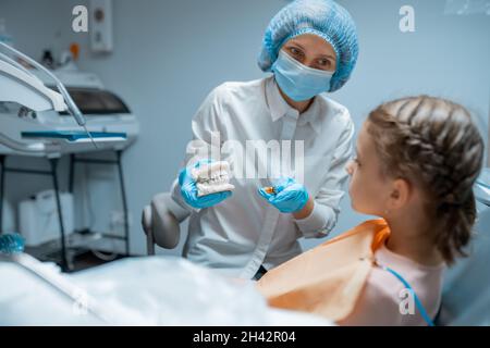 Kinderzahnärztin Frau zeigt kleinen Mädchen, wie sie ihre Zähne auf einem Modell des Kiefers richtig putzen können Stockfoto