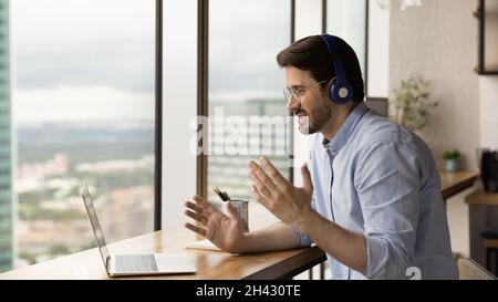 Glücklicher junger Mann mit Kopfhörern, der Videoanruf hält. Stockfoto