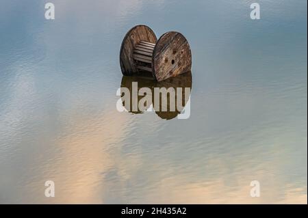 Ein hölzerner Kreis in einer großen Wasserpfütze mit einer Spiegelung des Himmels auf den kleinen Wasserwellen in der großen Wasserfläche Stockfoto