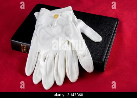 Weiße Handschuhe und bibel isoliert auf rotem Hintergrund Stockfoto