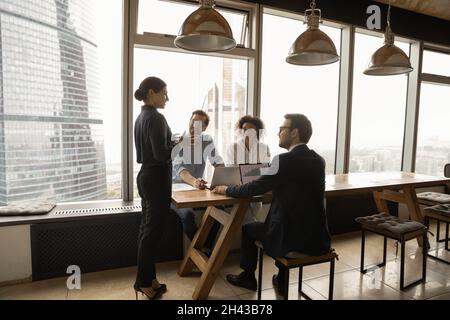 Glückliche junge Kollegen mit gemischter Rasse hören der weiblichen Führerin zu. Stockfoto