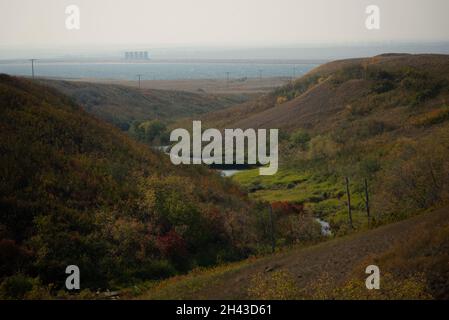 Eine breite Aufnahme von Hügeln mit bunten Herbstblättern bedeckt. Ein Rillbach zwischen den Hügeln, der in das Hintergrundwasser fließt Stockfoto