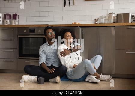 Glückliches junges gemischtes Rennpaar, das auf dem Boden in der Küche sitzt. Stockfoto