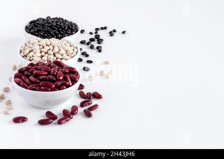 Auswahl an Bohnen in einer weißen Schüssel auf weißem Hintergrund. Rote Bohnen, weiße Bohnen und schwarze Bohnen Stockfoto