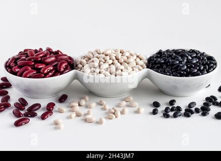 Auswahl an Bohnen in einer weißen Schüssel auf weißem Hintergrund. Rote Bohnen, weiße Bohnen und schwarze Bohnen Stockfoto
