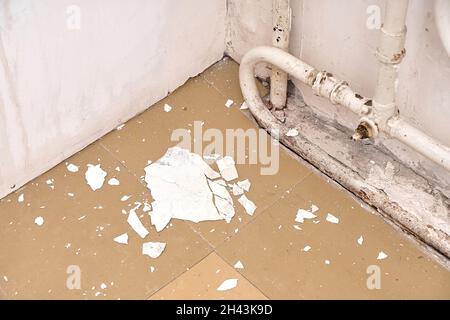 Das Innere ist ein altes Haus, das renoviert werden muss. Der zerbröckelnde weiße Putz von der Wand liegt auf dem Boden, in der Nähe des alten Heizkörpers. Stockfoto