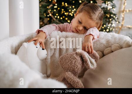 Nettes Kleinkind Kind wartet auf Geschenke zu Hause nach der Dekoration Weihnachtsbaum im Öko-Stil mit Holzspielzeug. Weihnachtsabend für Kinder. Nordischer Stil Stockfoto