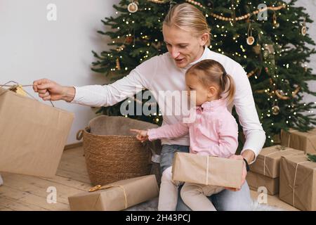 Vater mit Kind macht sich bereit für Weihnachten, Geschenkschachteln in der Nähe von Baum. Glückliche Familie träumt von Feiern und Geschenken bei stylish Stockfoto