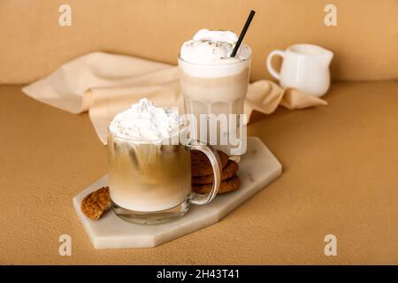 Glas und Tasse vereisten Hojicha Latte auf beigem Hintergrund Stockfoto