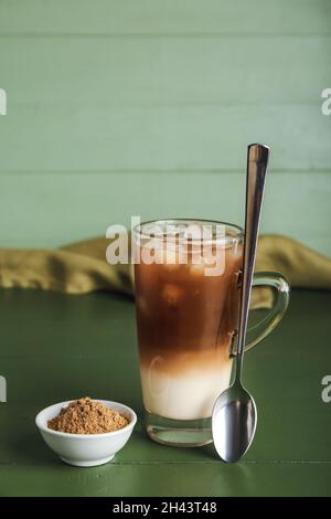 Glastasse aus vereisten Hojicha Latte und Pulver auf dem Tisch Stockfoto