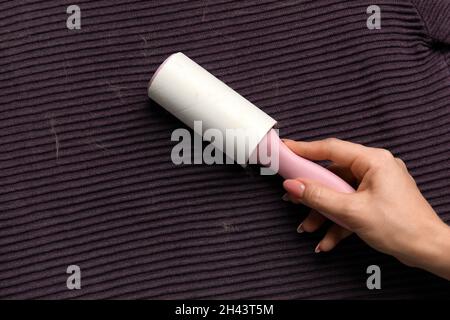 Frau, die ein lila Tuch mit Flusenrolle von Haustierhaaren putzt, Nahaufnahme Stockfoto