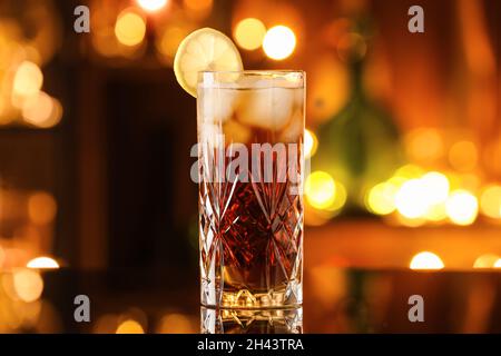 Ein Glas leckeren Cuba Libre Cocktail auf dem Tisch vor verschwommenem Licht Stockfoto