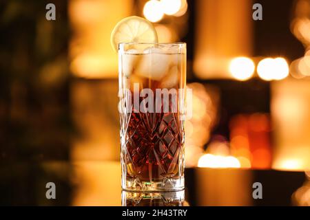 Ein Glas leckeren Cuba Libre Cocktail auf dem Tisch vor verschwommenem Licht Stockfoto