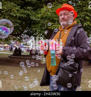 Ein Mann, der in einem Park steht, schießt Blasen aus zwei Blasengeschützen. Stockfoto